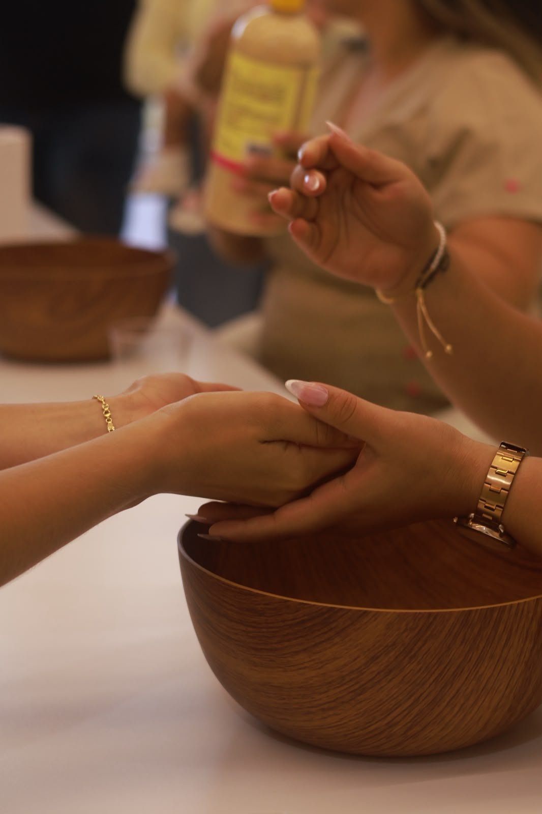 Manicurista atendiendo las manos de una clienta sobre un bol de madera